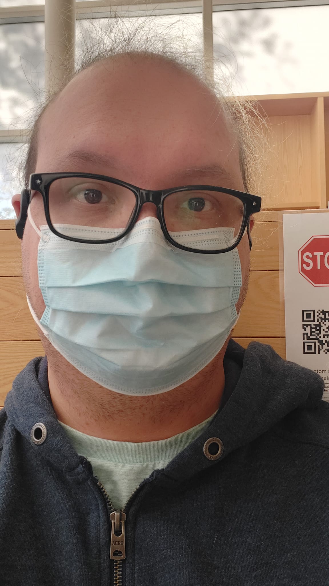 A man with thin green hair sits in a hospital waiting room